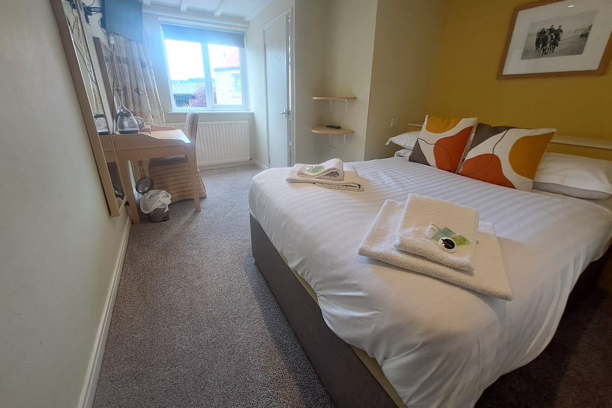 A hotel room with a large bed, a desk with a chair, a mirror, and a window.
