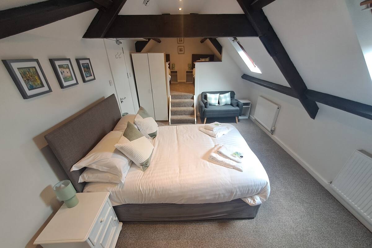 A bedroom with a large bed, a nightstand, a chair, and a wardrobe.