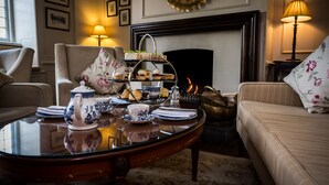 A cozy room with a fireplace, a three-tiered tea service, and a floral-patterned sofa. - Findon Manor Hotel (Worthing)