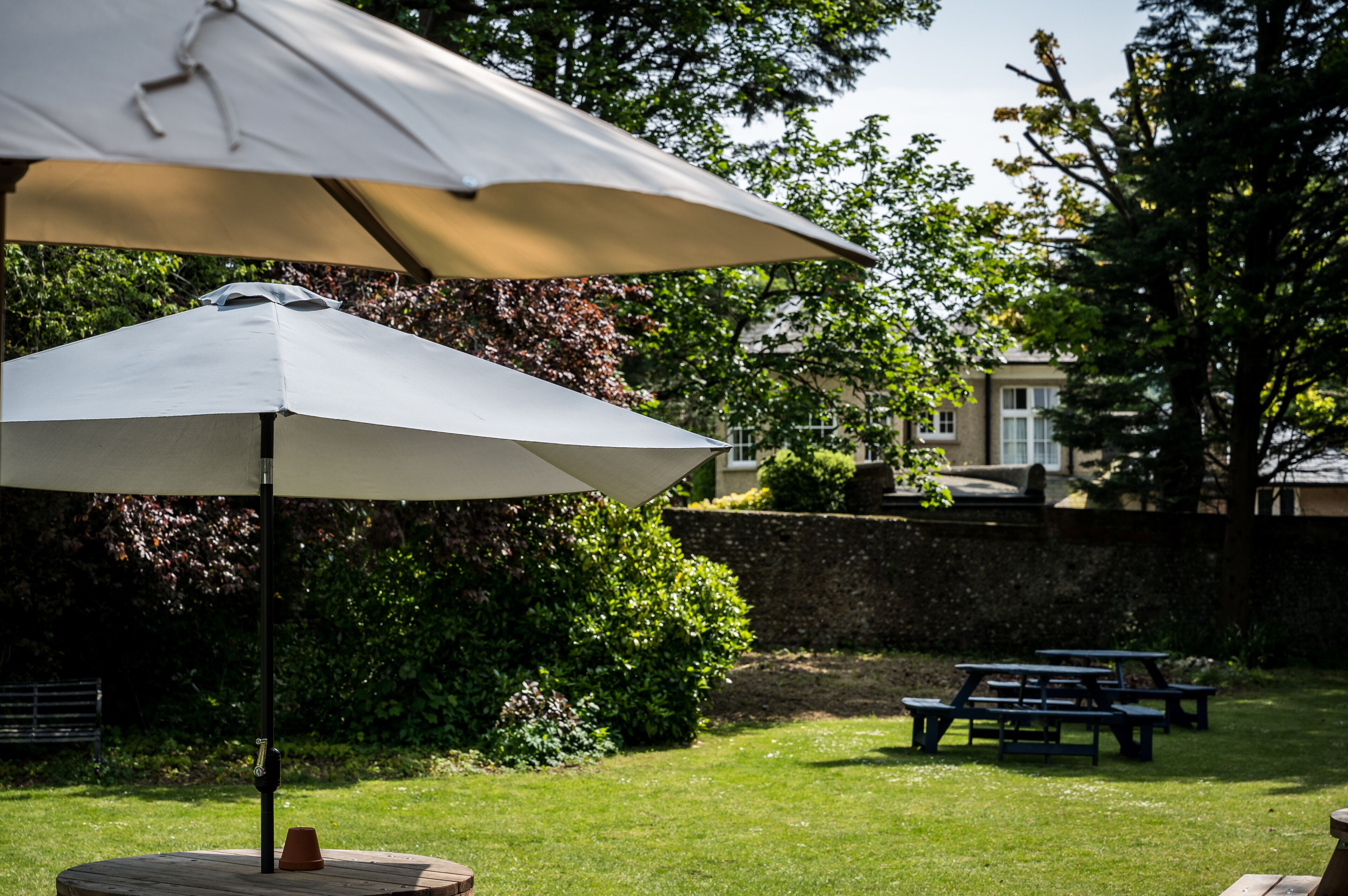 A patio area with a large umbrella, picnic tables, and a brick planter.