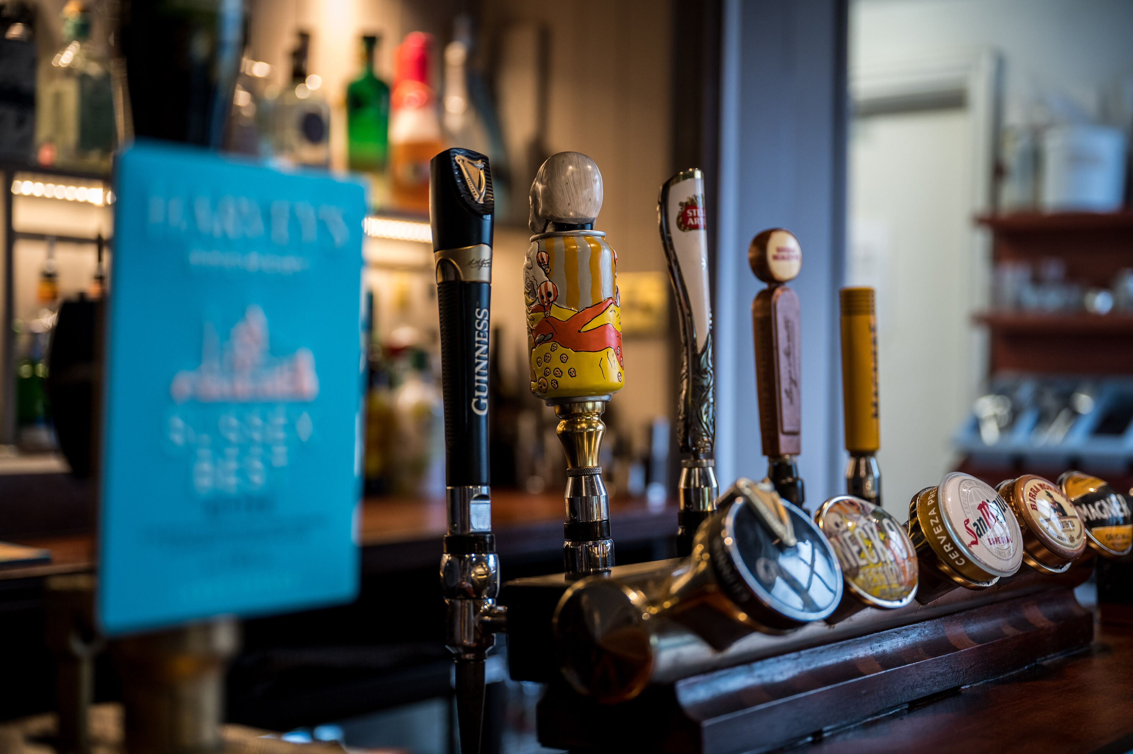Un bar con diferentes grifos de cerveza y botellas al fondo.