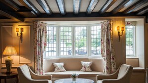 A cozy room with a bay window, a sofa, two armchairs, a table, and a lamp. - Findon Manor Hotel (Worthing)