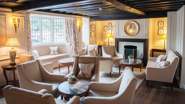 A traditional room with a fireplace, multiple seating areas, and a large window with curtains. - Findon Manor Hotel (Worthing)