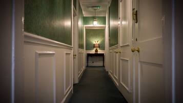 A hallway with white doors, green walls, and a lamp on a table at the end.