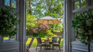 An open doorway leading to a patio area with a table and chairs, a large umbrella, and decorative plants. - Findon Manor Hotel (Worthing)