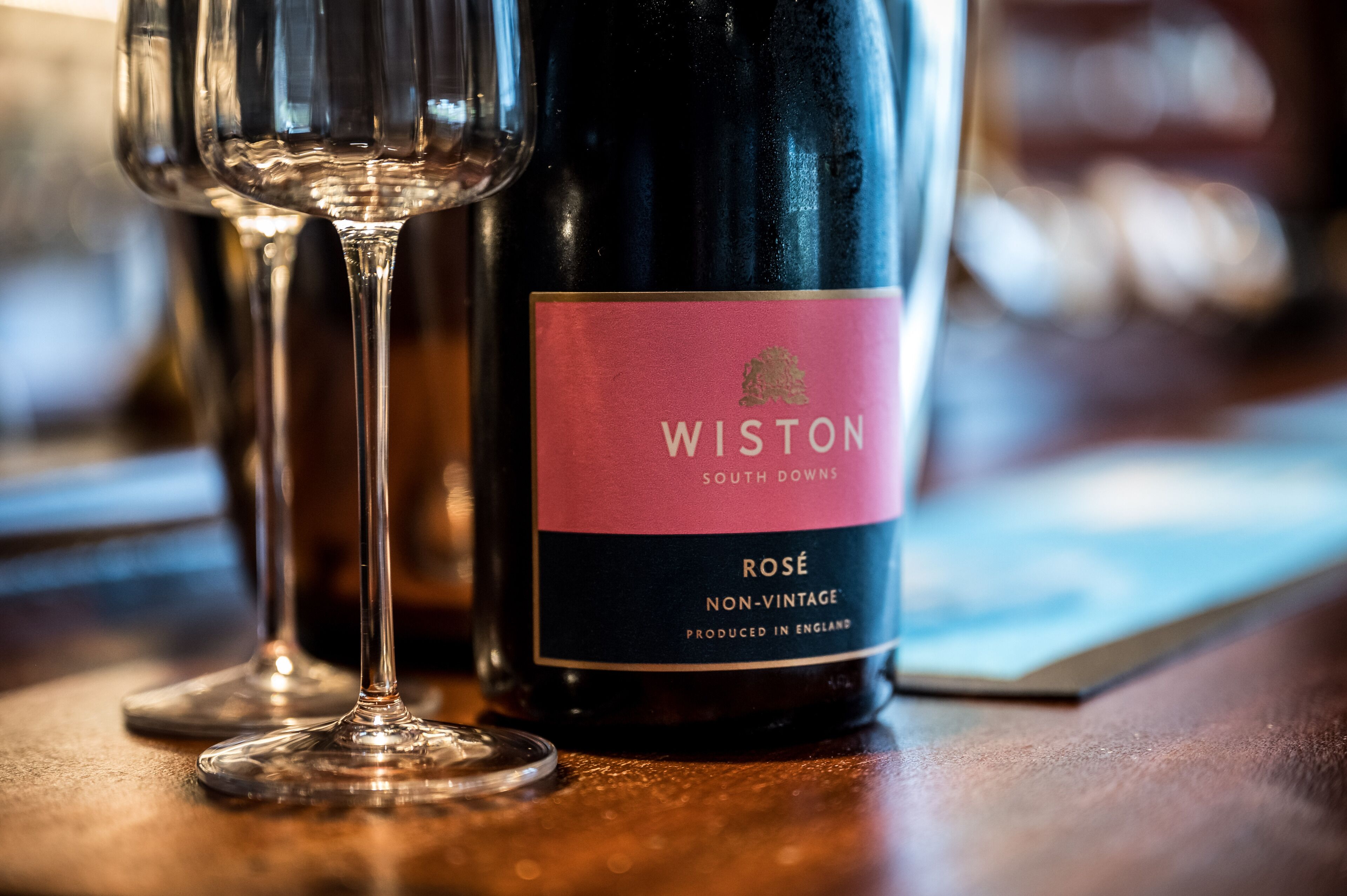 Une bouteille de vin rosé Wiston South Downs Non-Vintage et un verre à vin, posés sur une surface en bois.