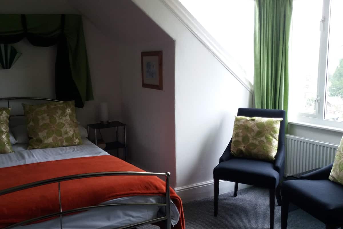 A bedroom with a bed, two pillows, a chair, a nightstand, a picture on the wall, and a window with curtains.