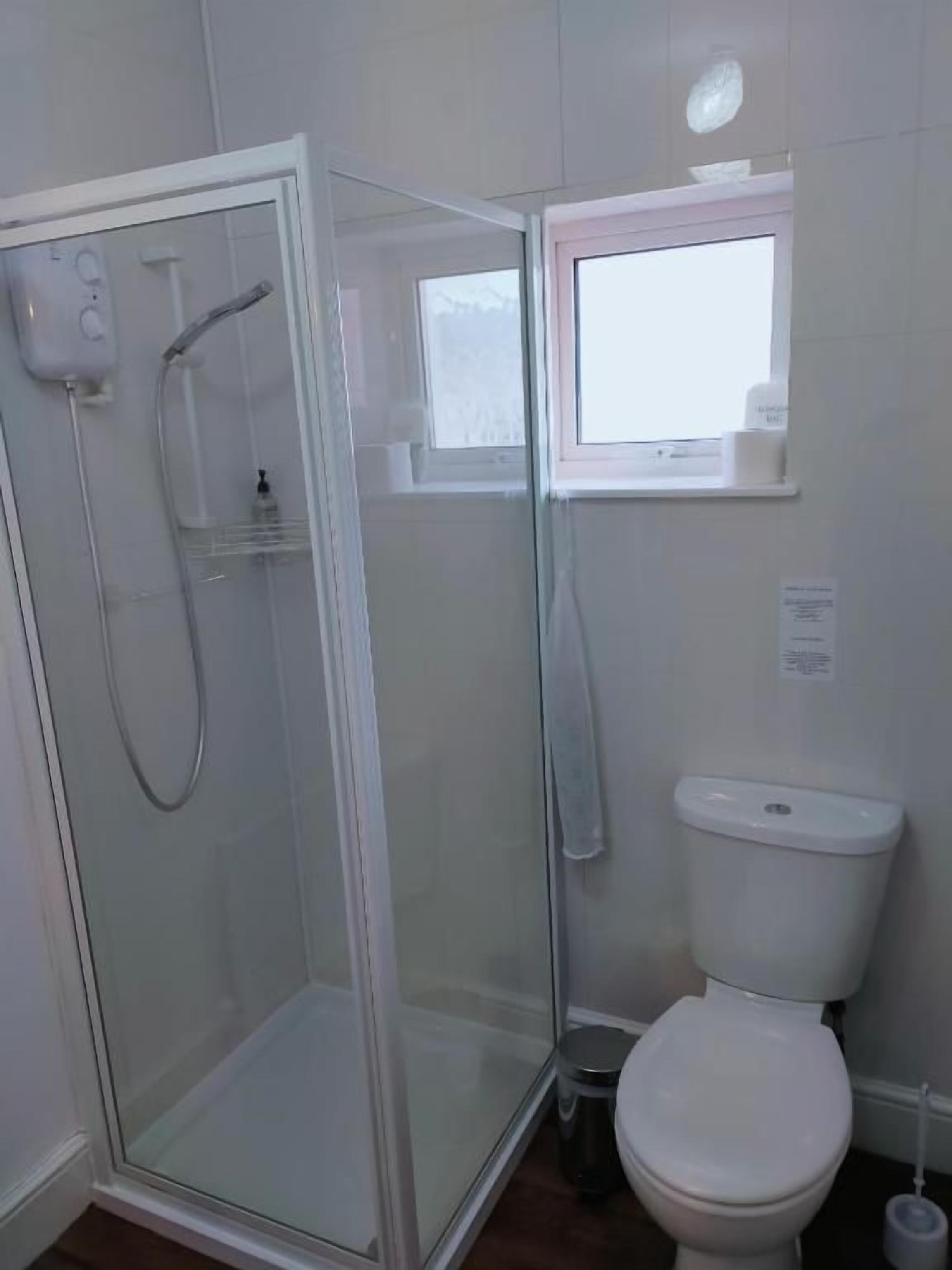 A bathroom with a glass-enclosed shower, a toilet, and a window above the toilet.