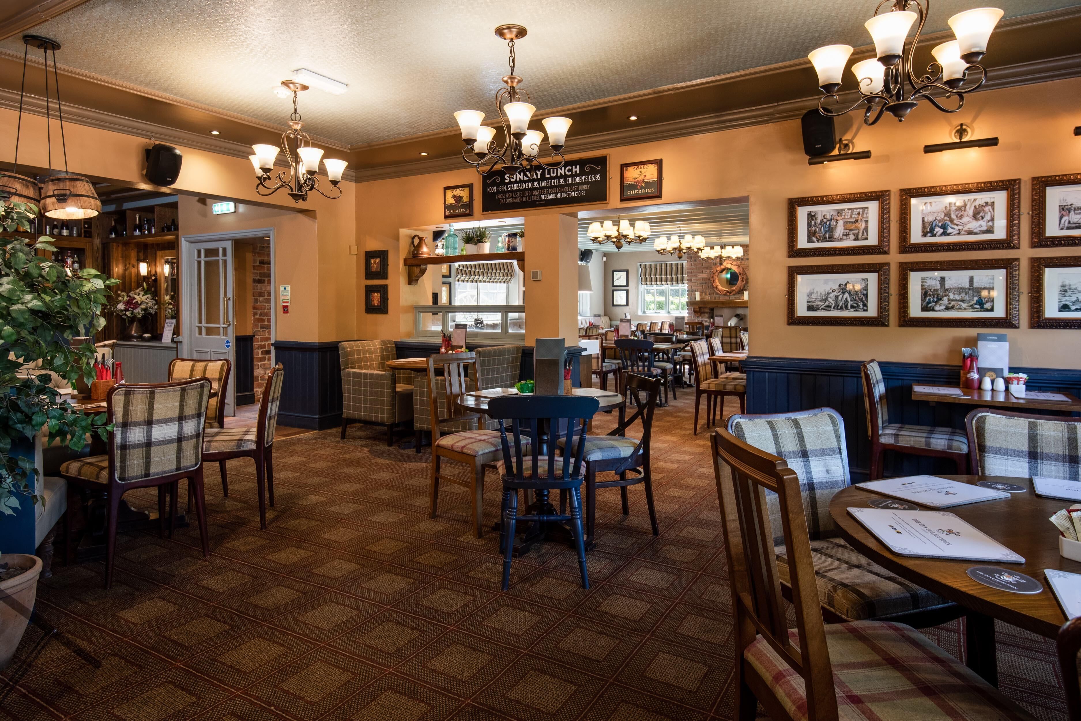 A restaurant with a patterned floor, wooden chairs, and tables. There are hanging lights and framed pictures on the walls.