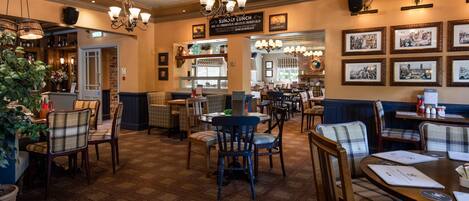 A restaurant with a patterned floor, wooden chairs, and tables. There are hanging lights and framed pictures on the walls.