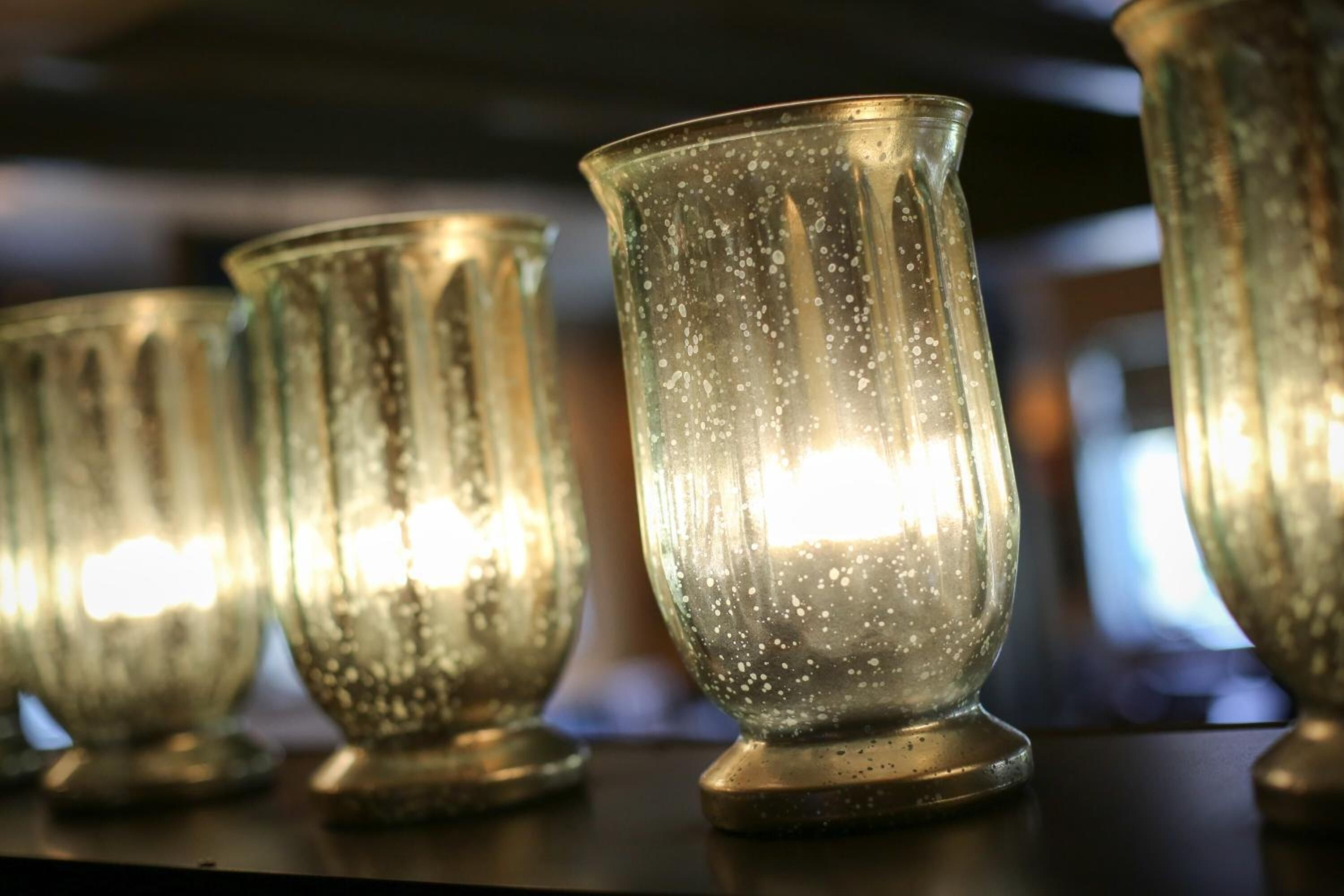 A row of clear glass candle holders with a warm light inside, placed on a dark surface.