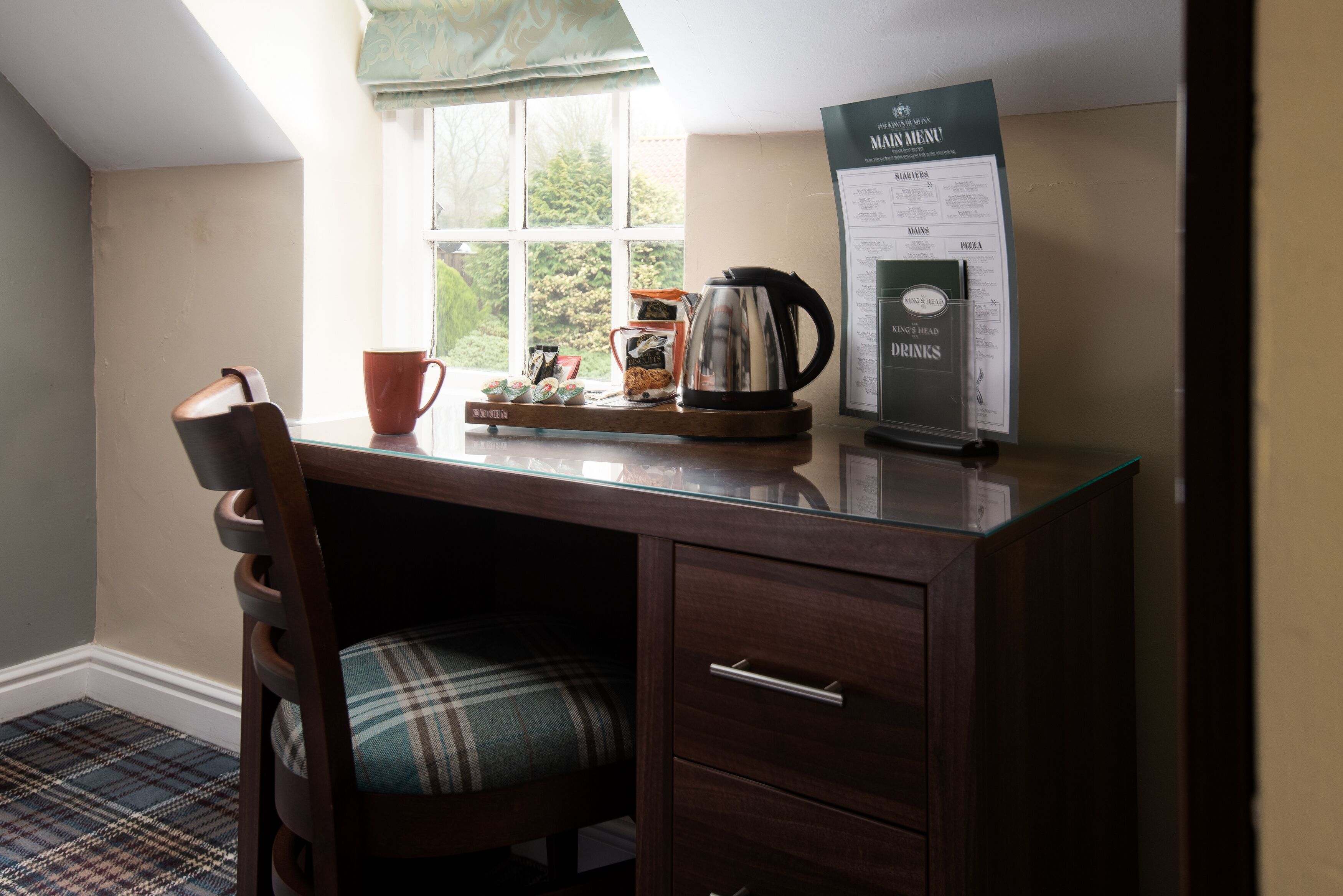 Een houten bureau met een geruit fauteuil, een koffiepot, een mok en een menubord.