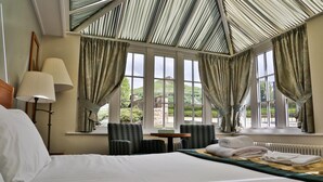 Ein Hotelzimmer mit einem großen Bett, zwei Sesseln, einem Tisch und Blick ins Freie durch große Fenster.
