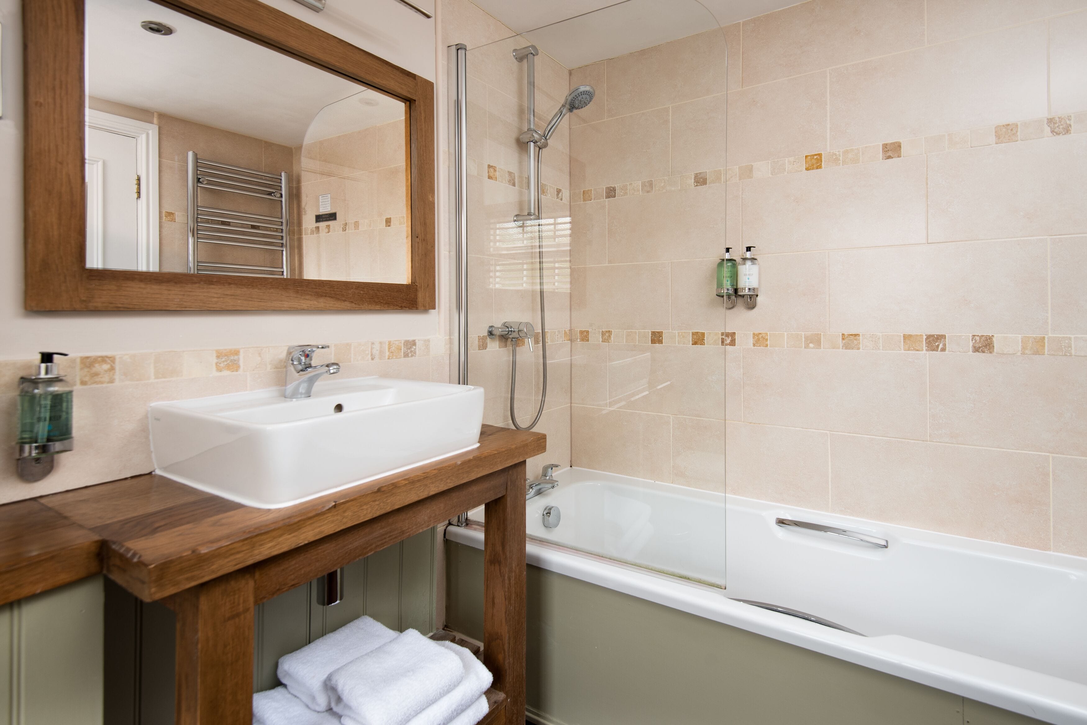 A bathroom with a wooden vanity, a sink, a mirror, a shower, and a bathtub.