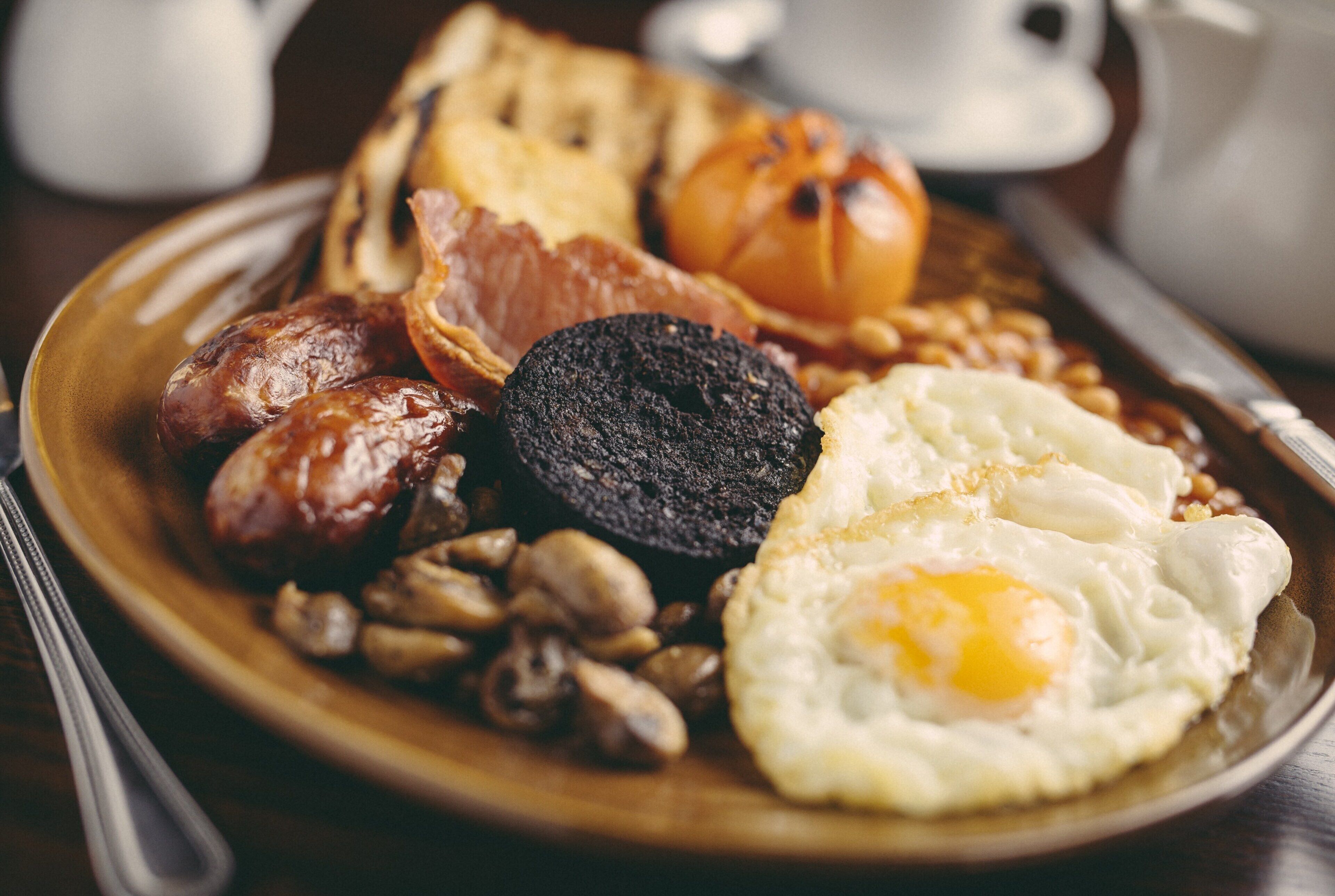 Prato de pequeno-almoço com enchidos, morcela, ovos fritos, cogumelos e torradas.