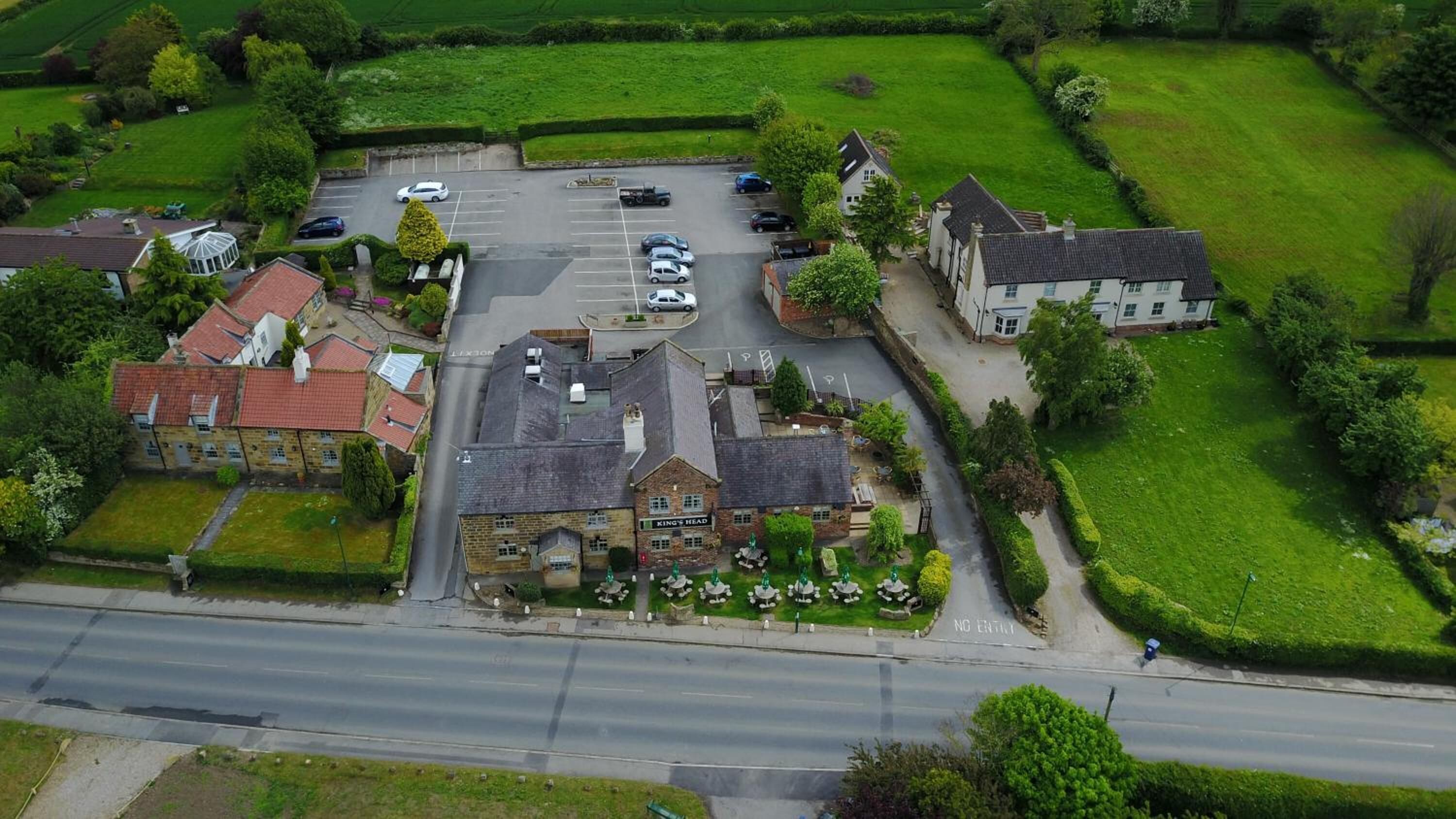 An aerial view of a rural area with a parking lot, a pub named 'King's Head', and surrounding greenery.