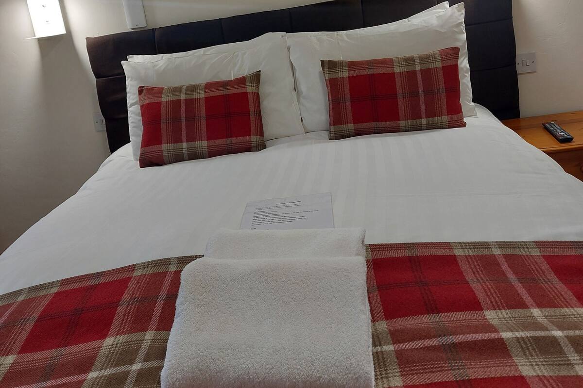 A neatly made bed with a plaid blanket and pillows, a framed picture on the wall, and bedside lamps.