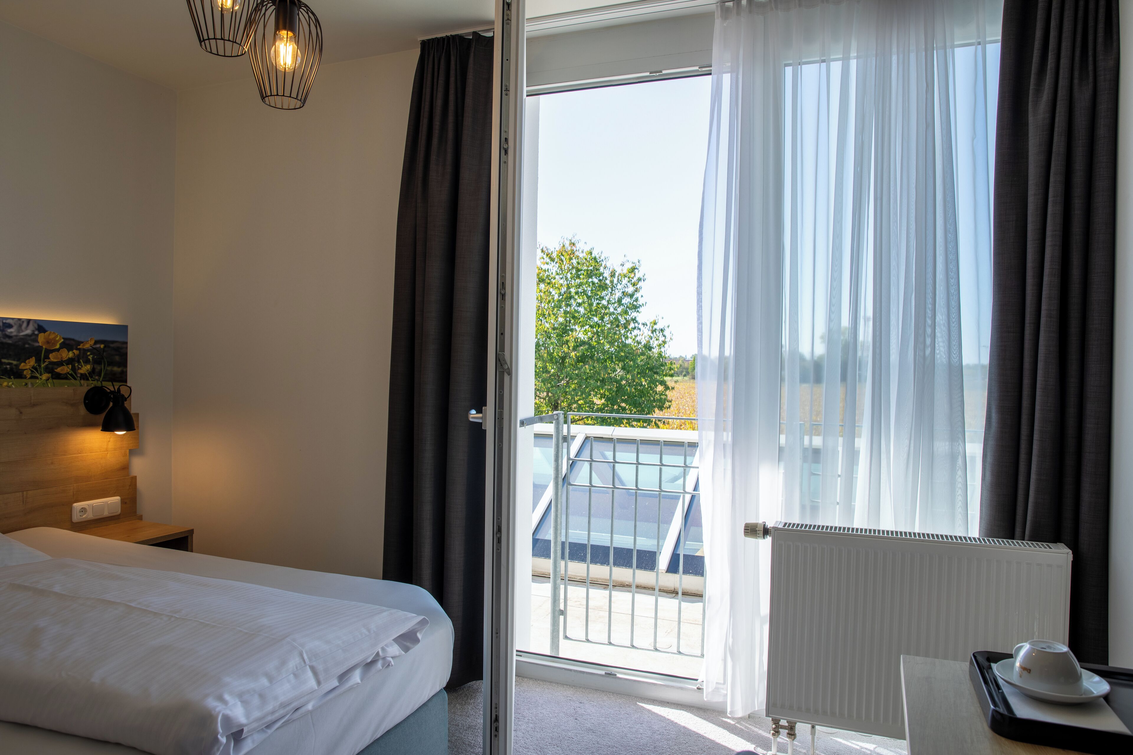 Et hotelværelse med seng, natbord, lampe, radiator og udsigt ud.