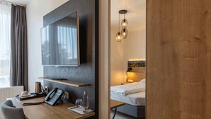 A modern hotel room with a flat-screen TV mounted on the wall, a wooden desk with a telephone and a glass, and a bed with a headboard lamp. - MEAT & STAY HOTEL (Haar)