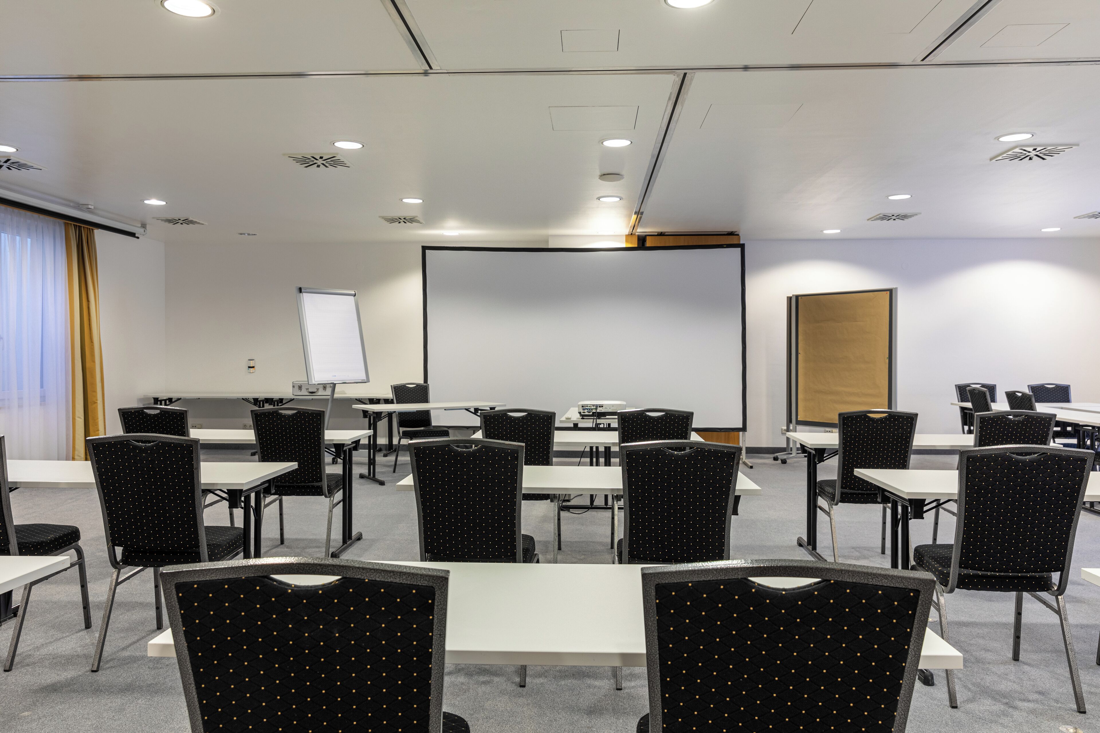 Ein Konferenzraum mit Tischen, Stühlen, einer Tafel und einer Projektionsleinwand.