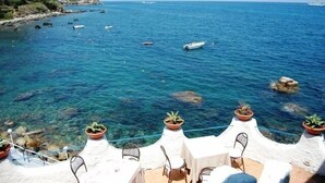 A seaside terrace with clear blue water, potted plants, and outdoor seating. - Villaggio Cirucco (Milazzo)