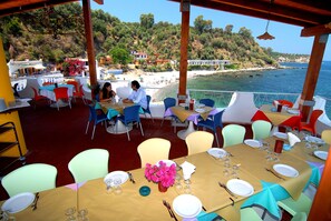 An outdoor dining area with tables set for two, overlooking a beach and the sea. - Villaggio Cirucco (Milazzo)