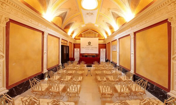 A long, ornate room with rows of chairs facing a central stage, likely used for events or conferences. - Palazzo Gattini Luxury Hotel (Matera)