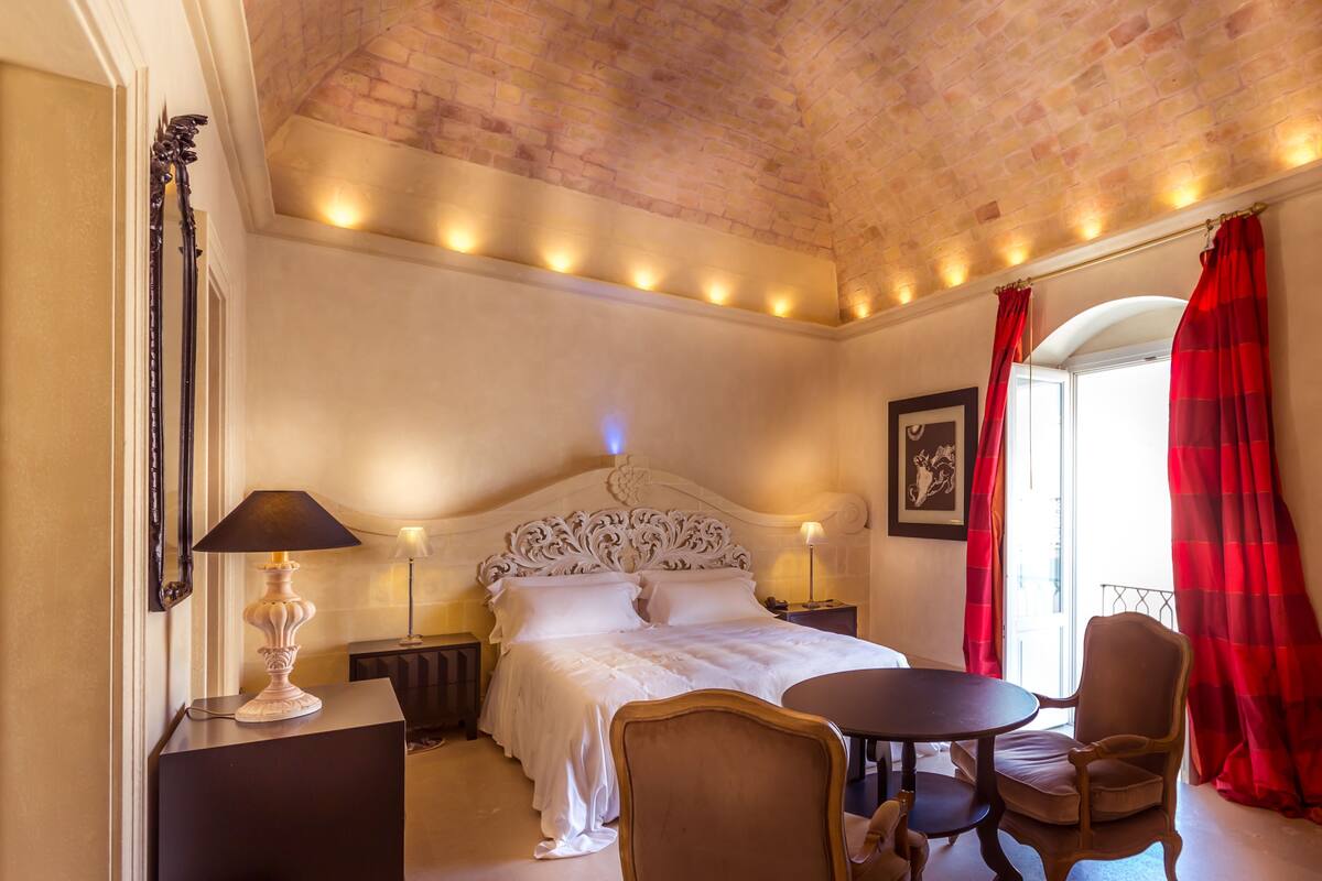 A bedroom with a large bed, a bedside table, a chair, and a small table.