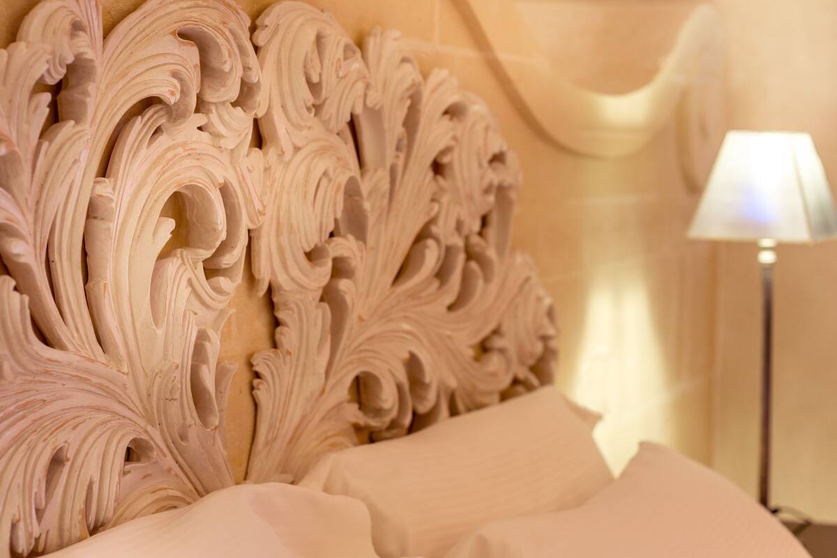 A bed with ornate headboard and a lamp on a bedside table.