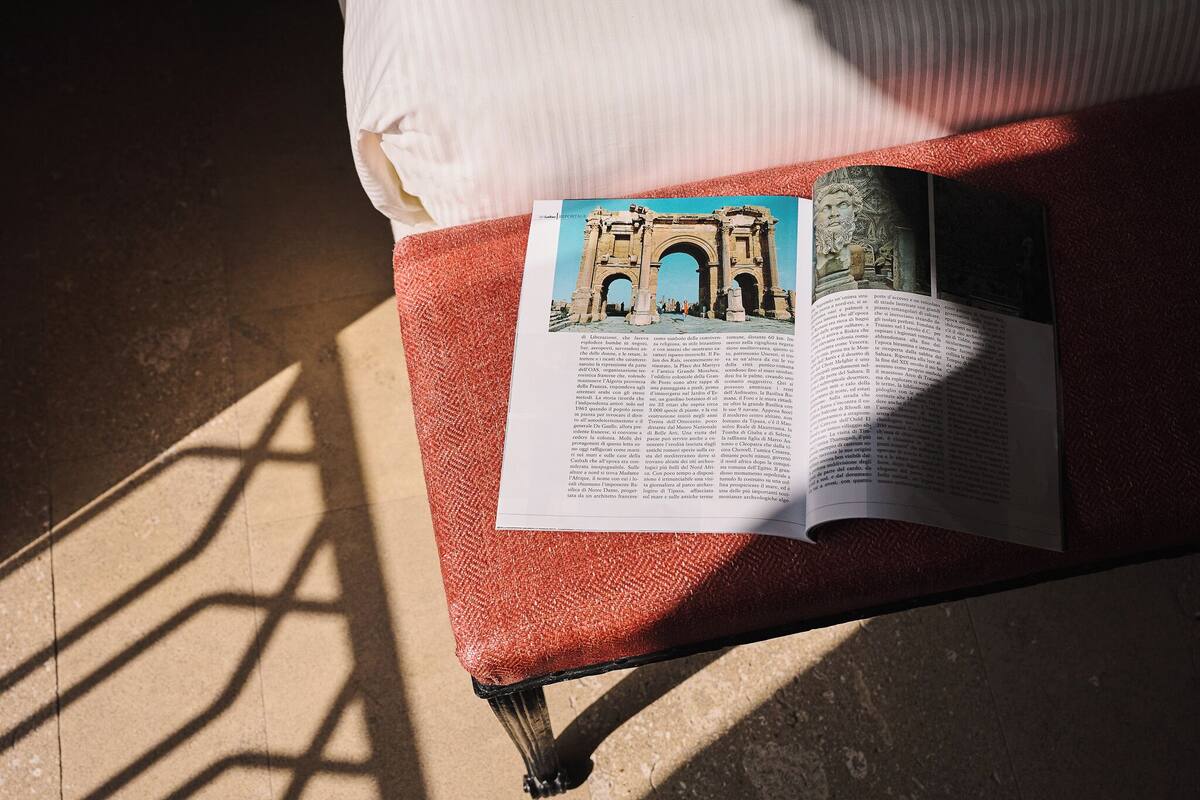 A book on a red cushioned bench with a view of an architectural structure.