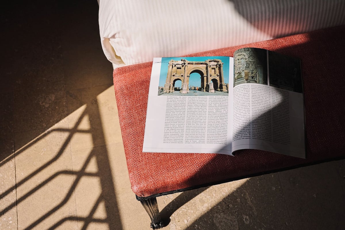 A book on a red cushioned bench with a view of an architectural structure.