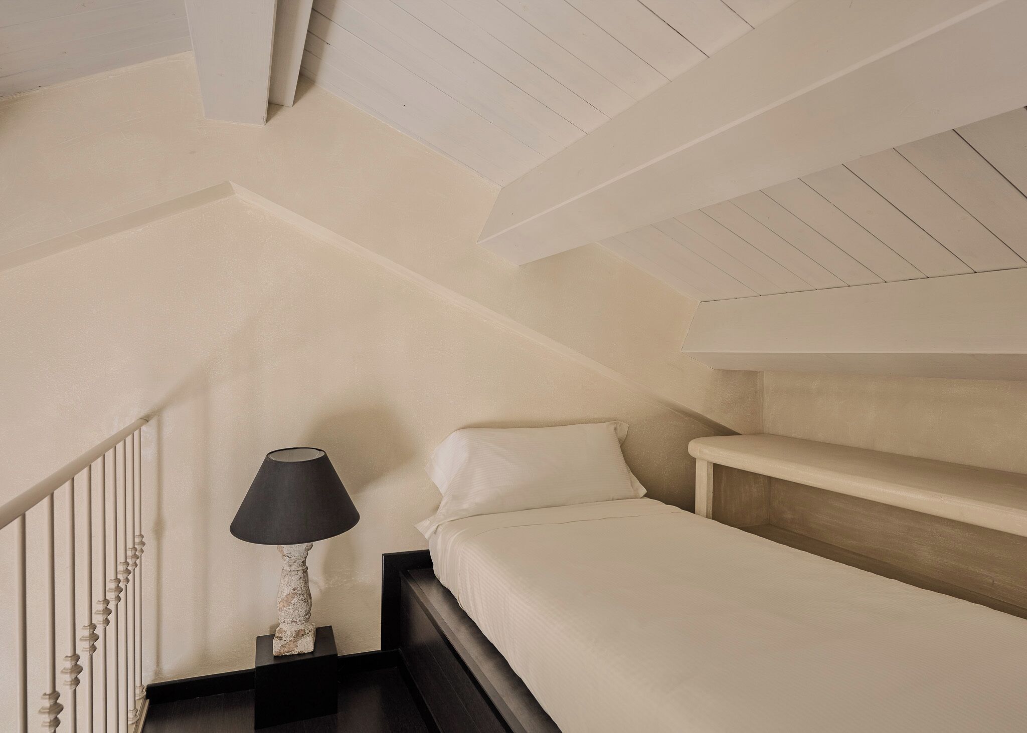 Une chambre à coucher avec un lit, une table de chevet, une lampe et un plafond en pente.