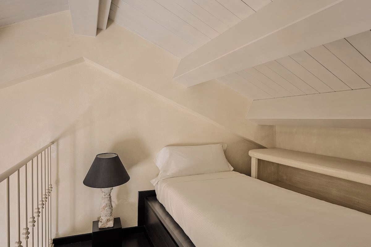A bedroom with a bed, a nightstand, a lamp, and a sloped ceiling.