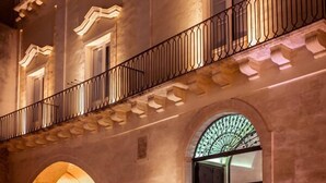 Un edificio histórico con una entrada abovedada, paredes de piedra y un balcón con barandilla de hierro forjado.