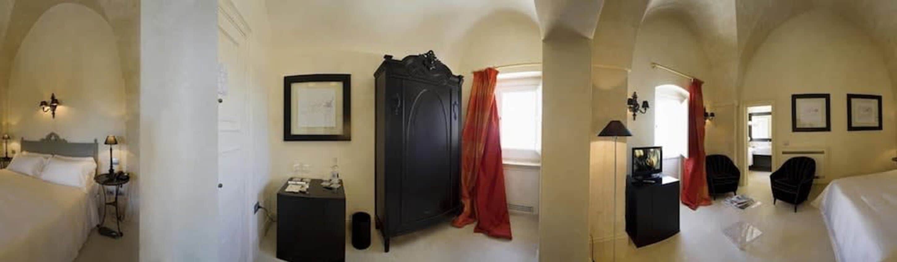 A hotel room with a bed, a small table with a lamp, a wardrobe, and a mirror.