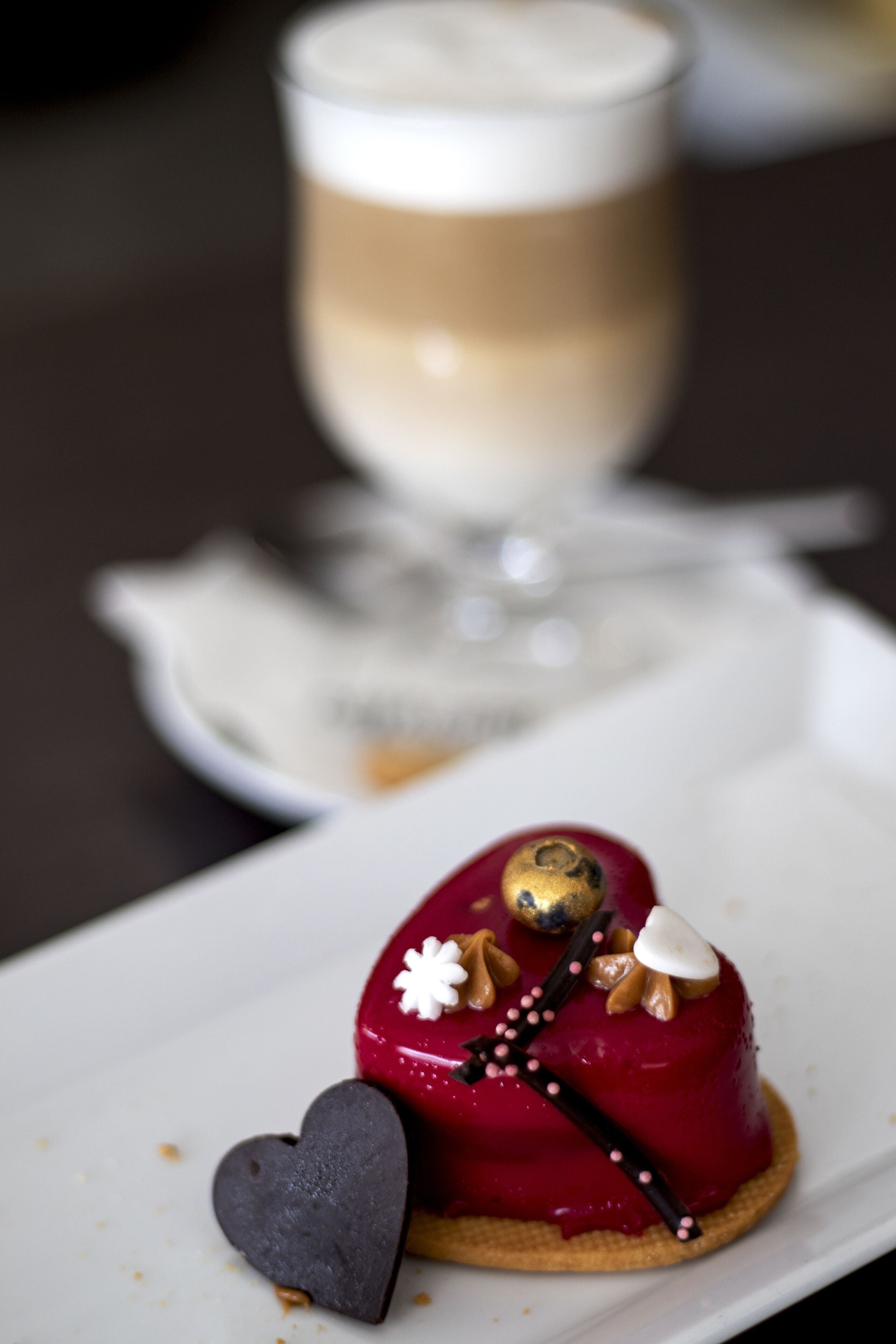 Un dessert su un piatto bianco, con un pezzo di cioccolato a forma di cuore accanto.