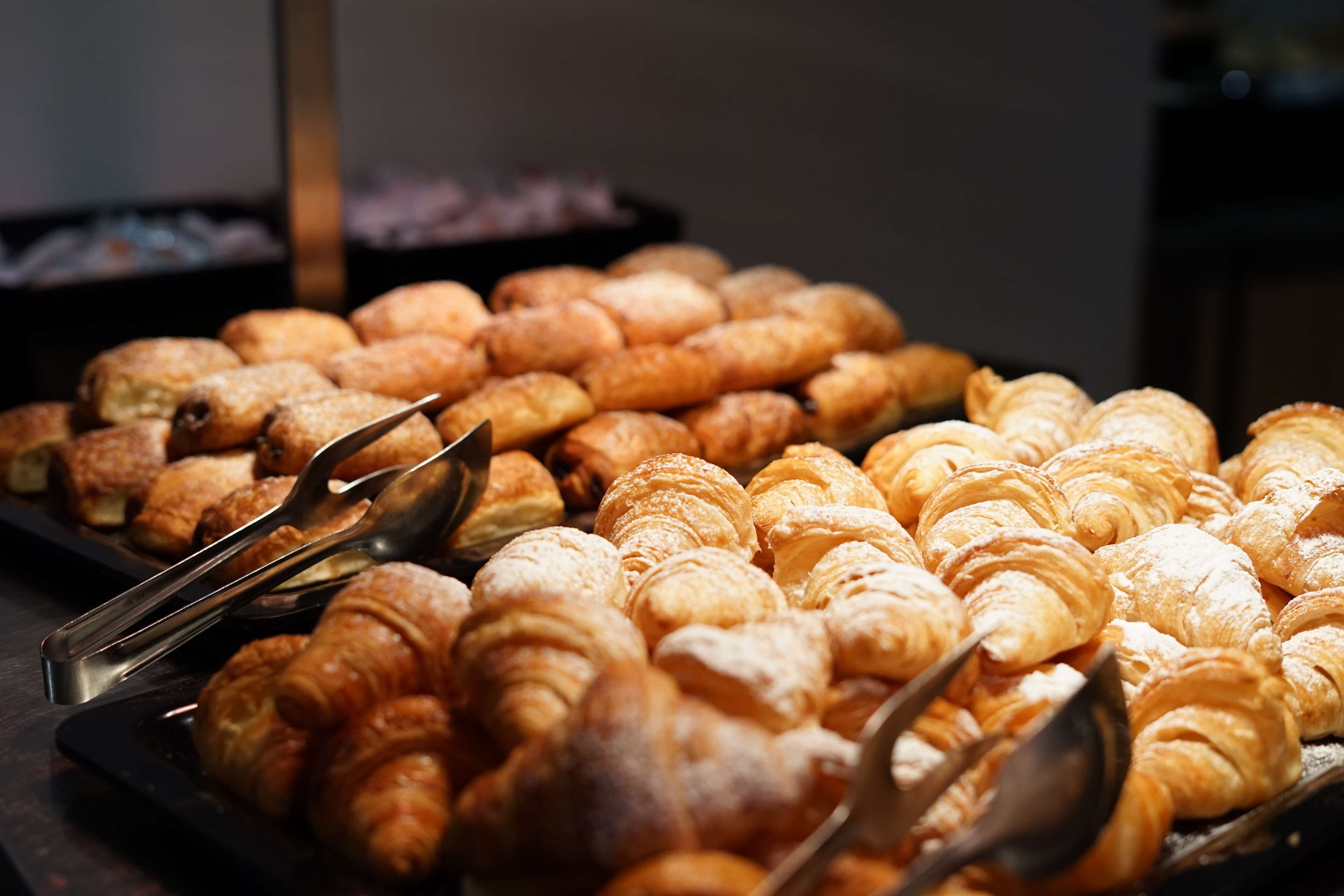 A variety of pastries displayed on trays, with tongs for serving.