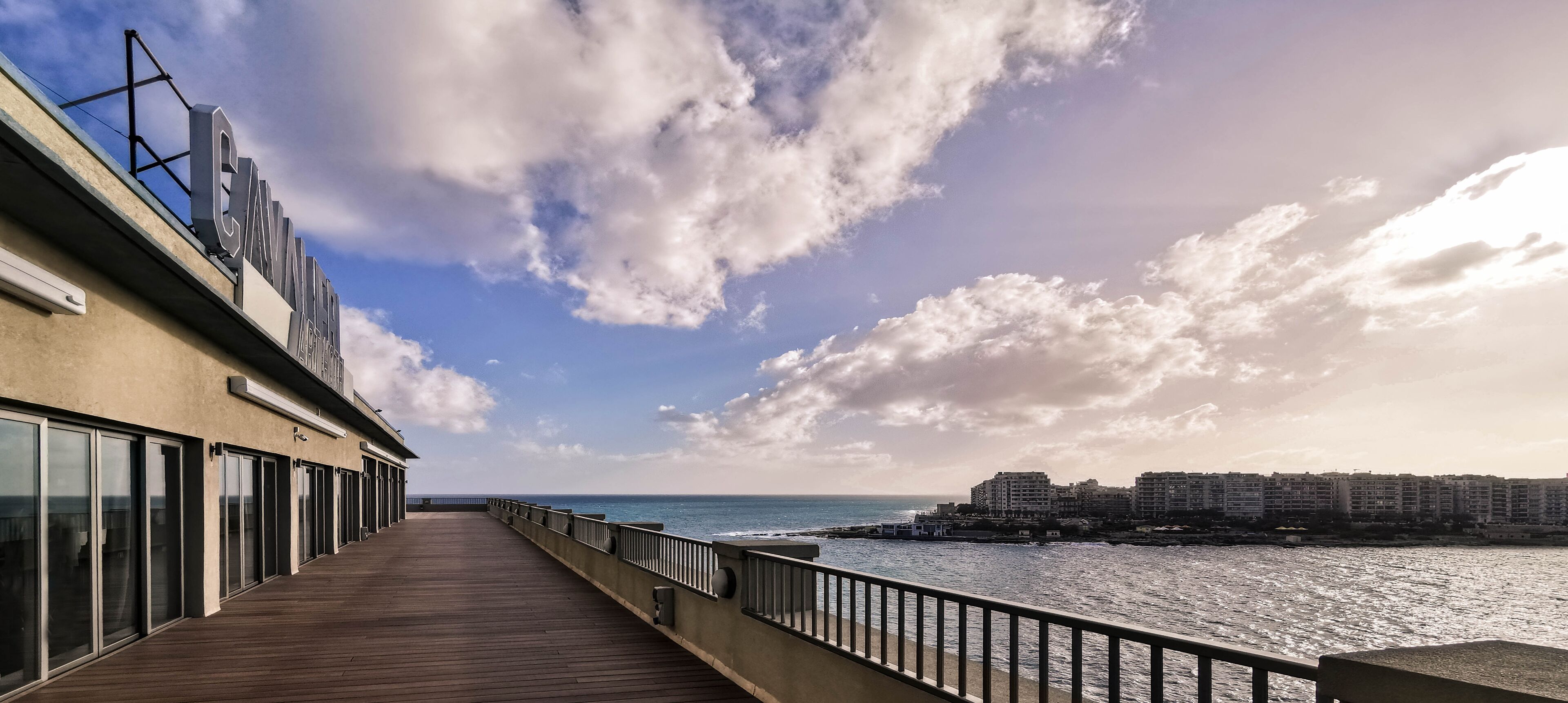 A wooden deck with a view of the ocean and buildings in the distance.
