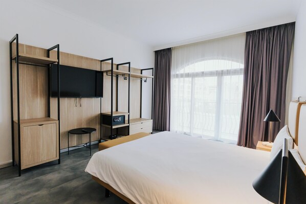 Habitación de hotel con cama, televisión montada en una pared de madera, escritorio con silla y ventana con cortinas.