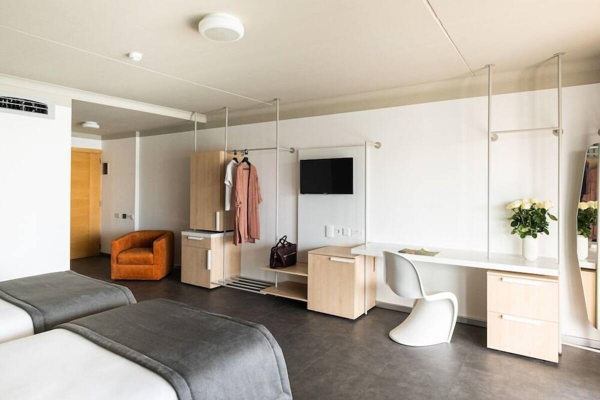 Una habitación de hotel moderna con cama, escritorio, silla, armario y televisor.