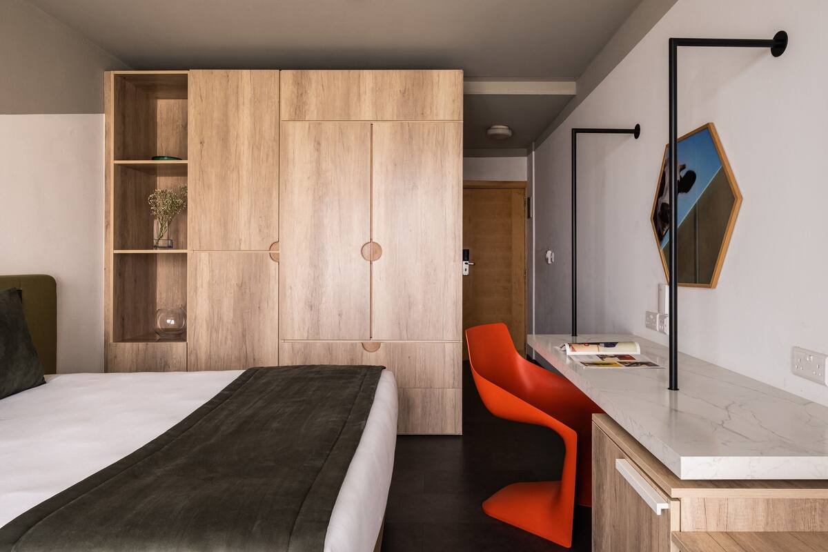 Un dormitorio moderno con cama, armario de madera, escritorio con silla y espejo.