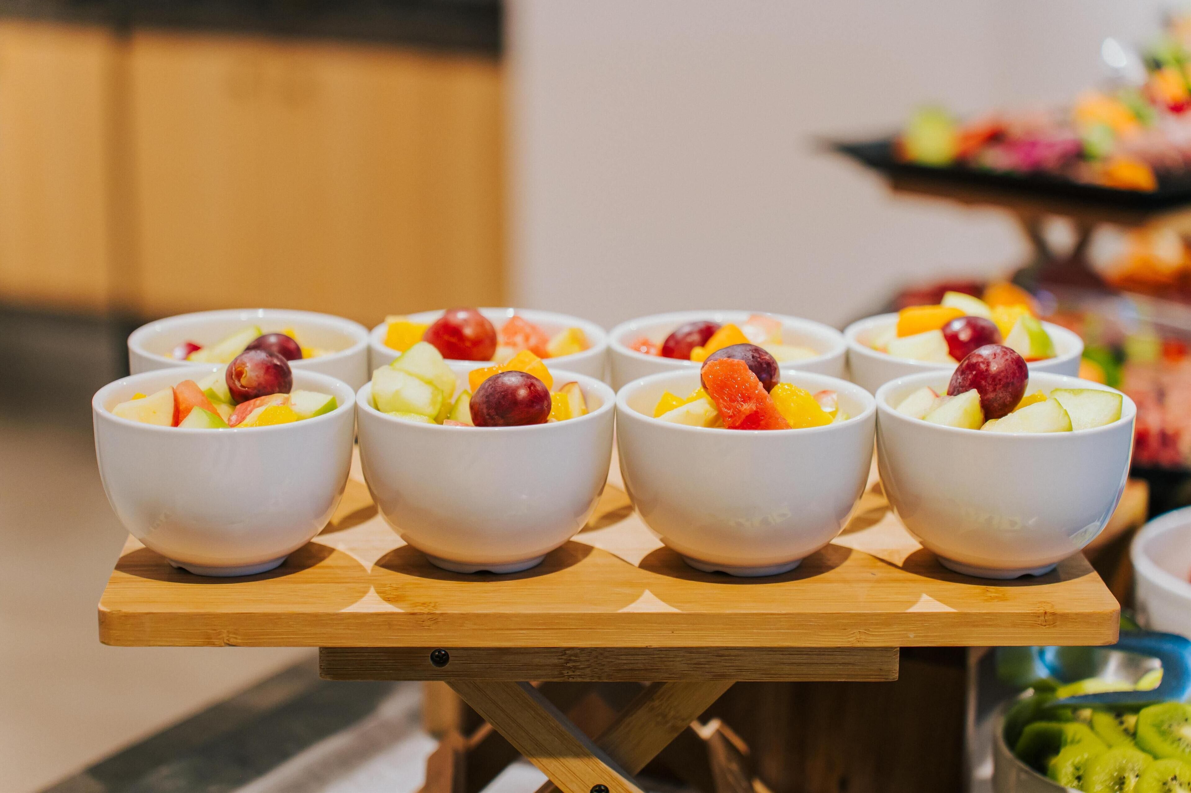 Een tafel met zes witte kommen met fruitsalade, op een houten tafel gezet.