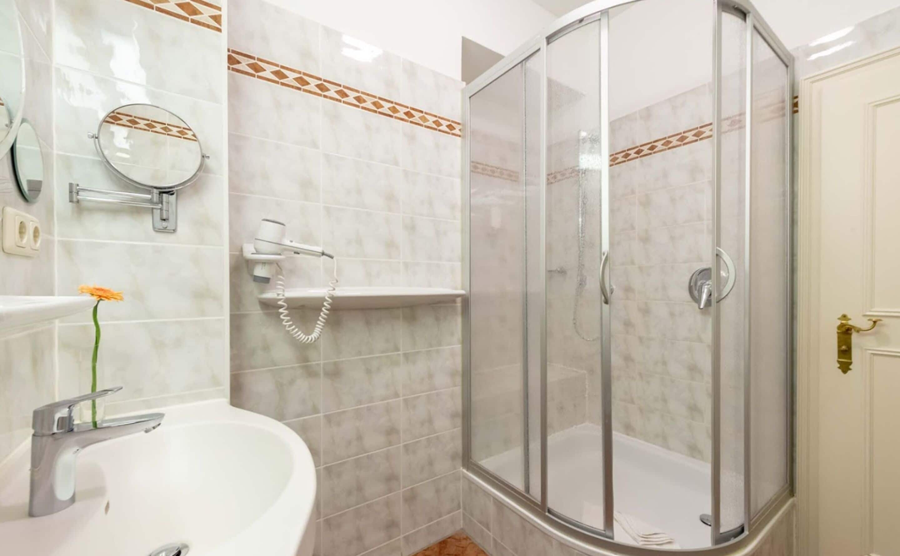 Ein Badezimmer mit einem weißen Waschbecken, einem Spiegel, einem Haartrockner und einer Dusche mit Glastür.