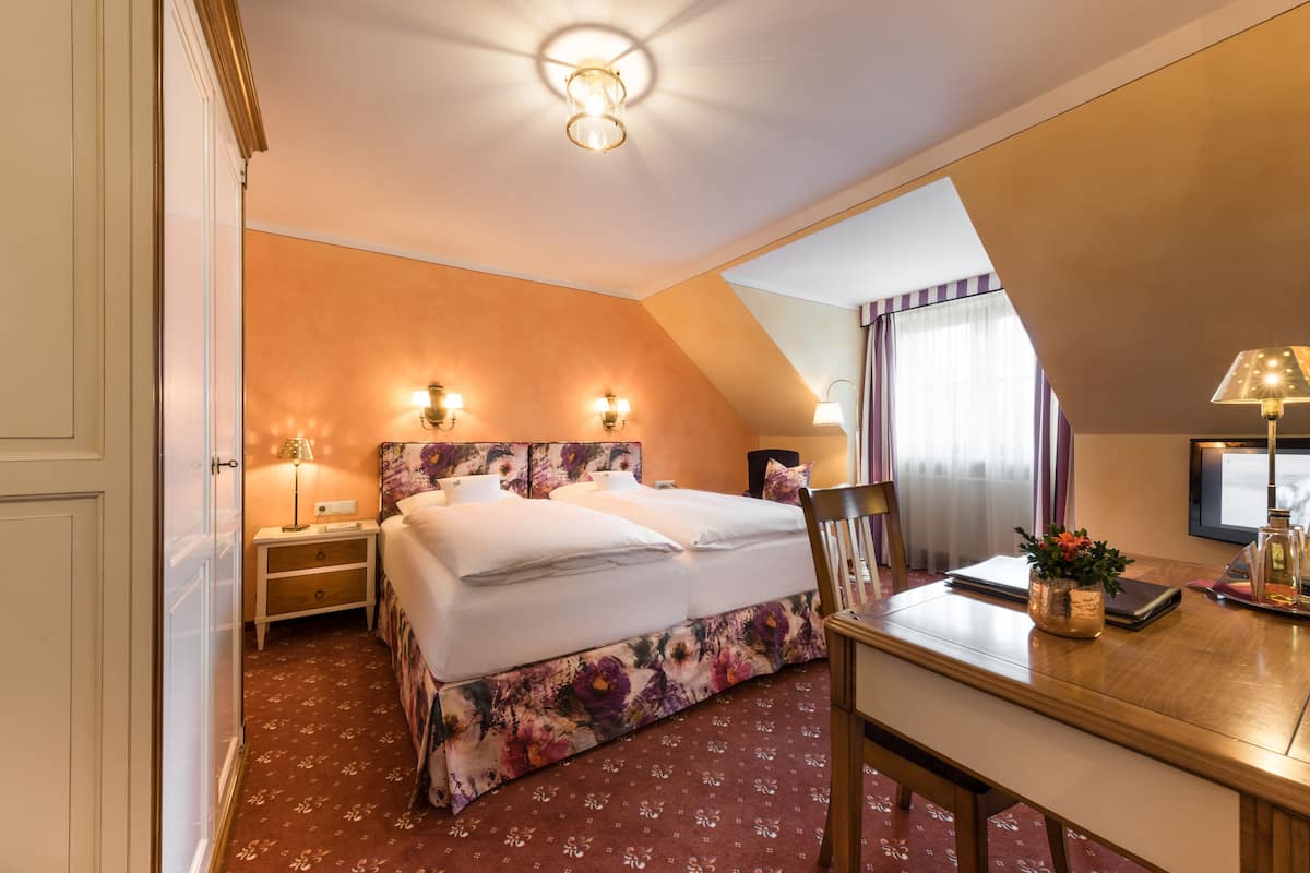 A hotel room with a large bed, two bedside tables, a desk with a chair, and a window with curtains.