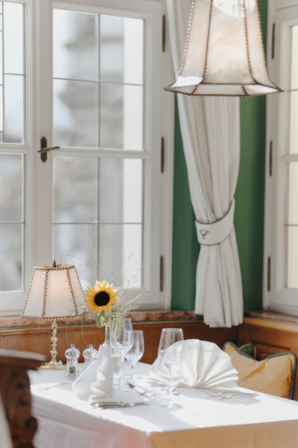 A dining table set with white tablecloth, plates, and glasses, a vase with a sunflower, and a hanging lamp.