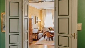 A room with green walls, a wooden floor, a dining area with a table and chairs, and a door leading to another room. - Romantik Hotel zur Post (Fuerstenfeldbruck)