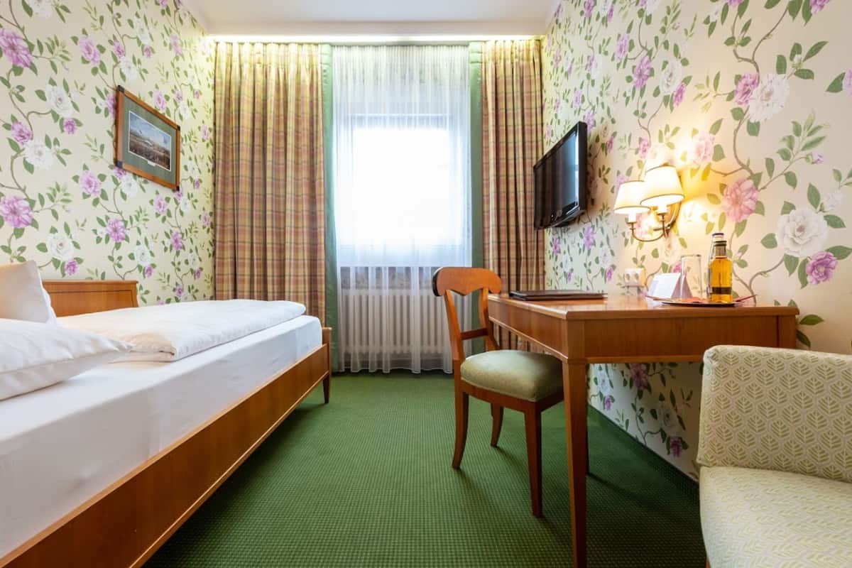 A hotel room with a bed, a desk with a chair, a television, and a window with curtains.
