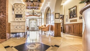 A lobby with a checkered floor, a reception desk, striped chairs, and a large vase with flowers. - Romantik Hotel zur Post (Fuerstenfeldbruck)