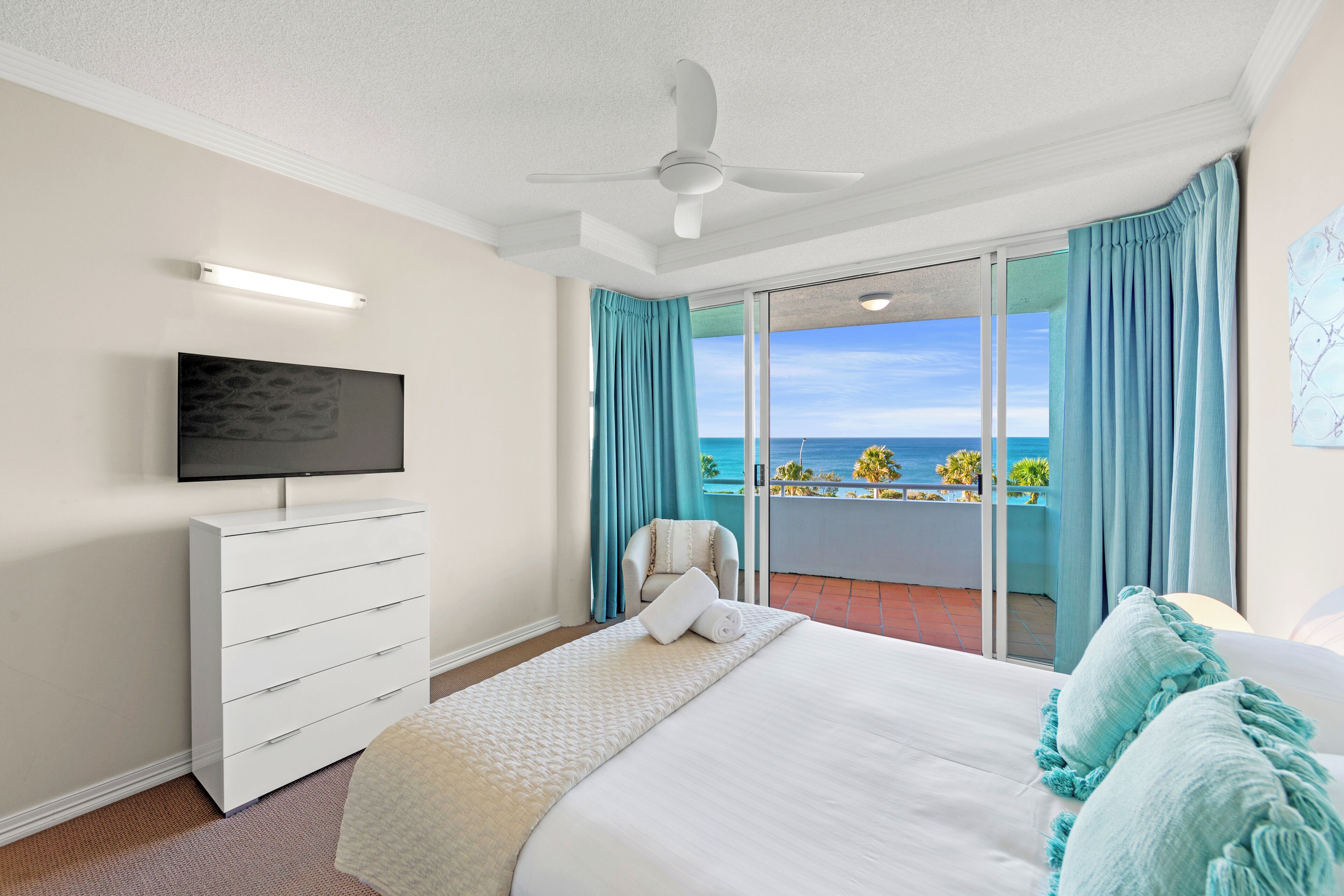 Habitación de hotel con cama, televisión, cómoda y balcón con vista al océano.