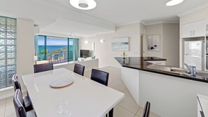 A modern kitchen with a dining area, a view of the sea, and a large window. - Alexandra on the Pacific (Alexandra Headland)